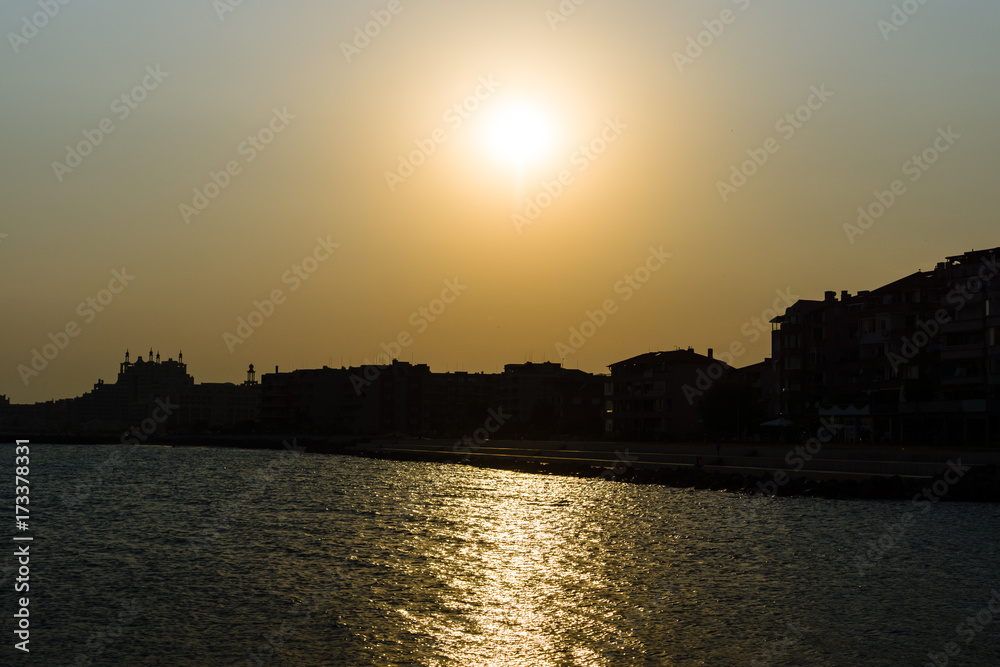 Sunset at the sea. Silhouettes of buildings on the beach in backlight.