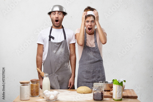 People, culinary, facial expressions and unexpectedness concept. Young male and female cookers being in panic as see how much they should cook for tomorrow, doesn`t know what to do, stare at camera