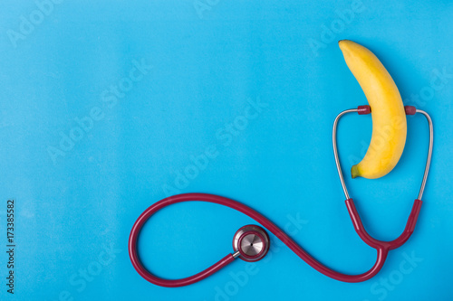 Stethoscope and yellow banana on blue background. For men penis check up concept. With empty free space for text or design. Top view