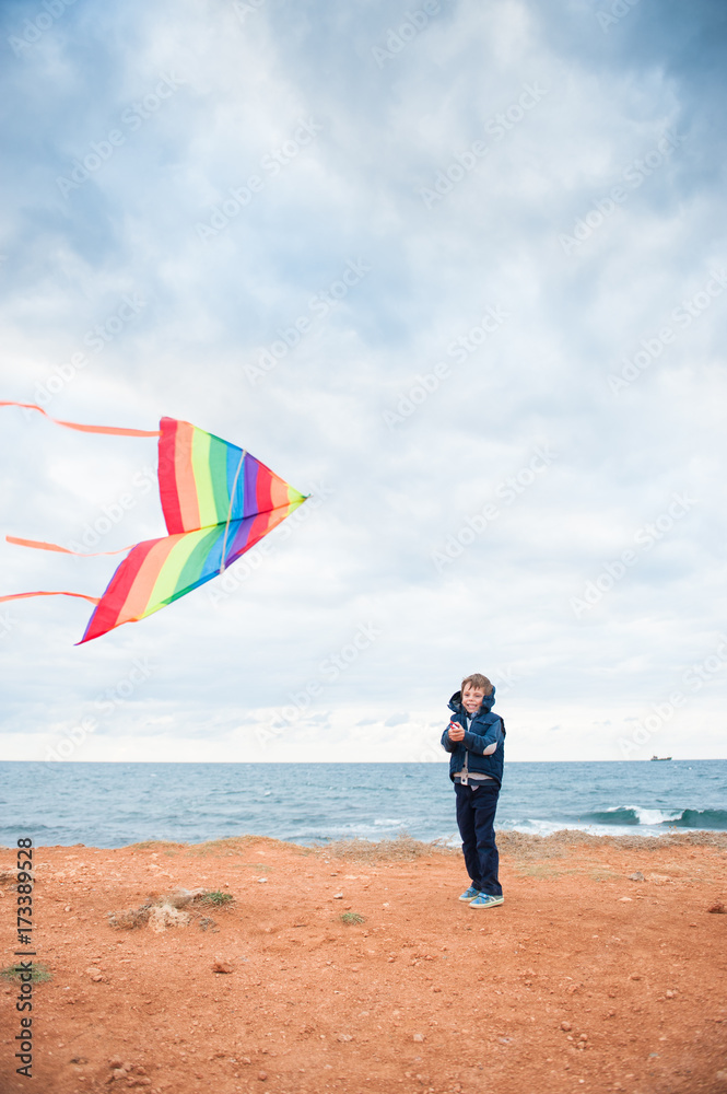 Obraz premium cute little boy plays with a kite on the ocean coast in cold weather
