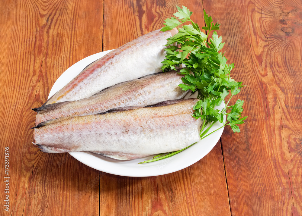 Uncooked carcasses of the Alaska pollock and parsley on dish Uncooked carcasses of the Alaska pollock and parsley on dish