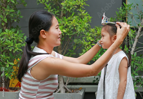 Mother wearing crown on head of little girl in the garden.