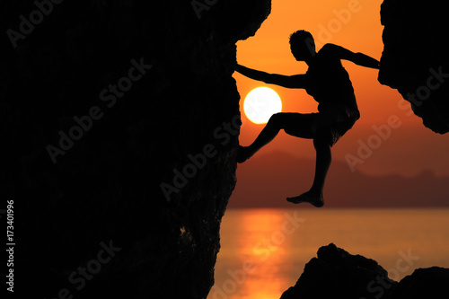 Silhouette of climber on a cliff against beautiful red sky sunset
