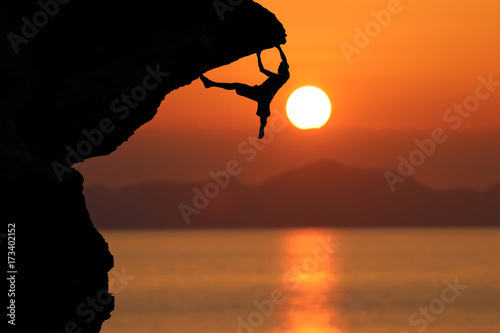 Silhouette of climber on a cliff against beautiful red sky sunset