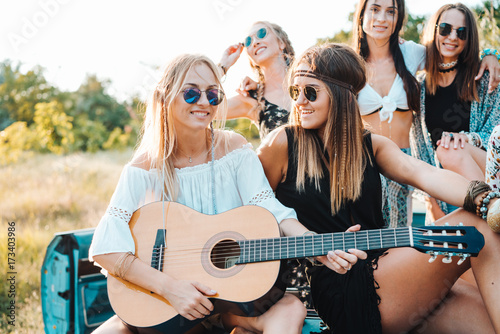 Girls are sitting on the trunk with a guitar