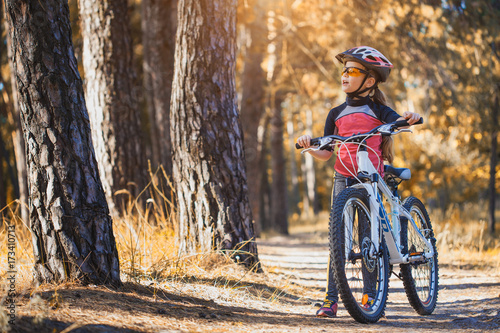 kid on a bicycle in the sunny forest. girl cycling outdoors in helmet