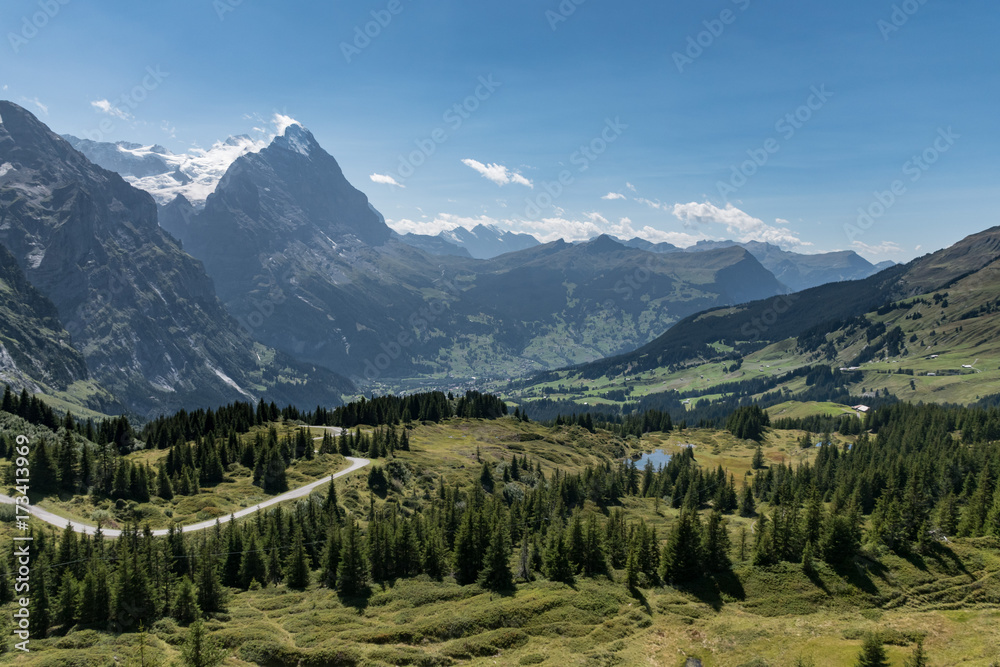 View from Grosse Scheidegg to the Grindelwald valley, Swiss Alps, with Eiger peak visible in clouds, and a road turn, lake and sparse forest in the meadows in the foreground