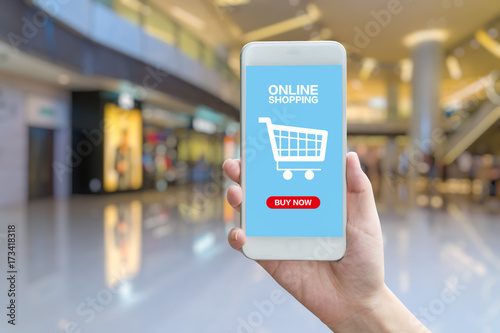 hand holding smartphone against blur bokeh of shop background with word online shopping buy now