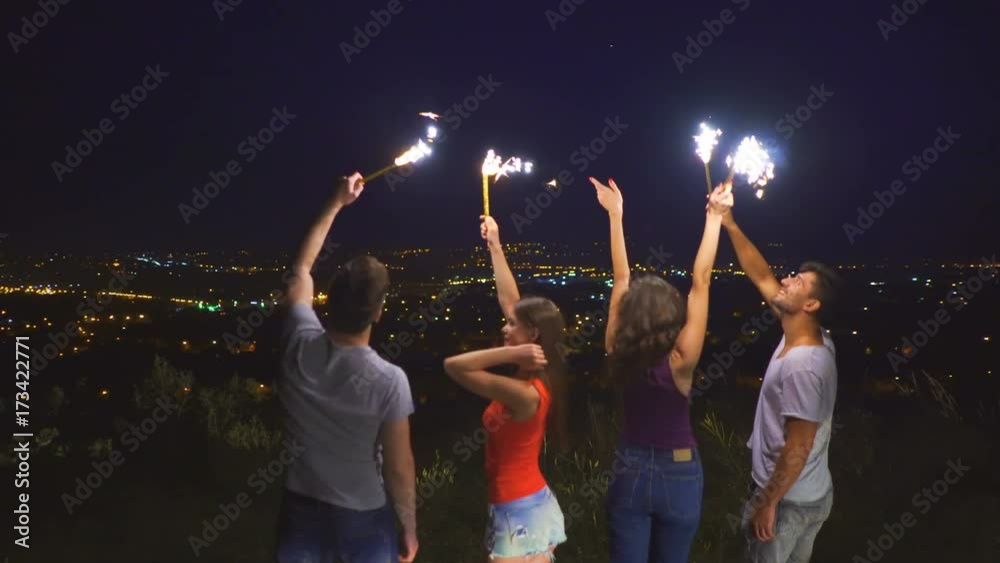 The young people with firework sticks dancing on the city background. night time