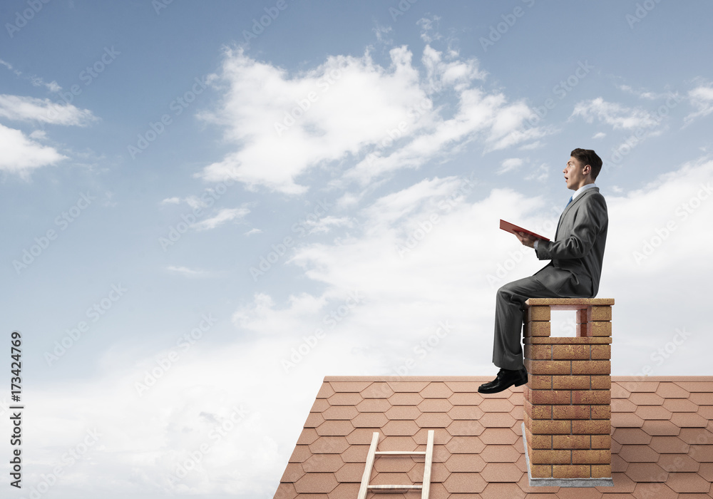 Student guy in suit on brick house roof reading book Student guy in suit on brick house roof reading book