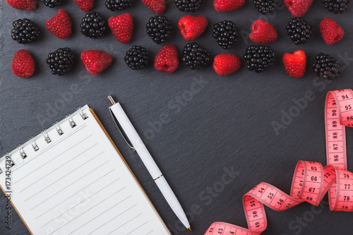 Red raspberries, tape measure, notebook and a pen on the black slate stone background photo