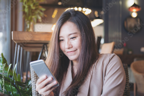 Closeup image of a beautiful Asian business woman holding , using and looking at smart phone in modern cafe