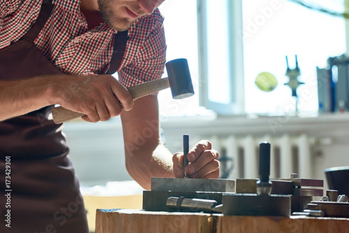 Bilde på lerret Closeup  of young man working with metal  in workshop, forming it with mallet on