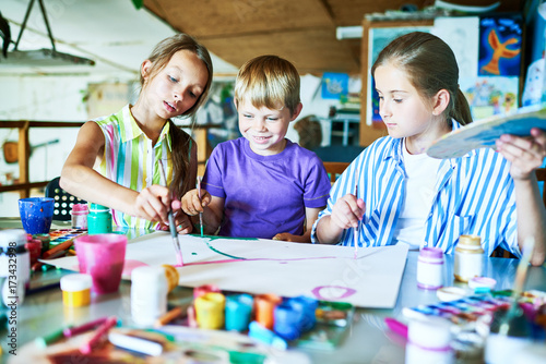 Portrait of three children painting picture together smiling happily while working in art studio during lesson