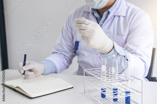 Scientist or medical in lab coat holding test tube with reagent, mixing reagents in glass flask in laboratory research