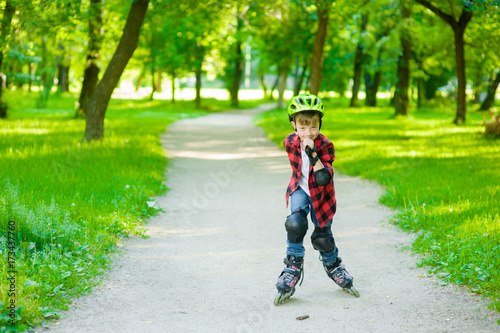 Young boy learn to roller skate in summer park. Space for text.