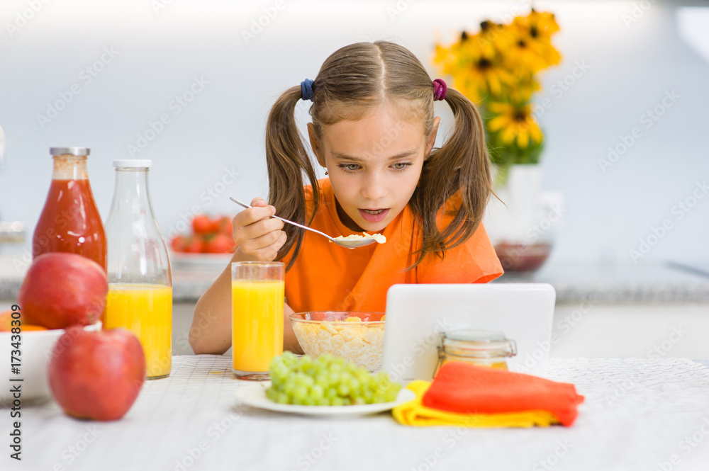 Little girl is having breakfast while watching the movie on the tablet Little girl is having breakfast while watching the movie on the tablet