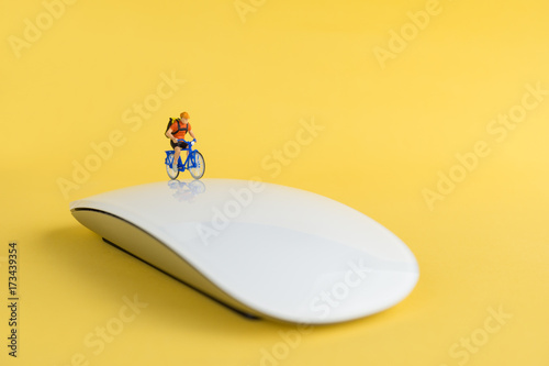 Work and exercise or work-life balance Concept. Miniature Figures Ride Bicycle on Mouse with yellow background