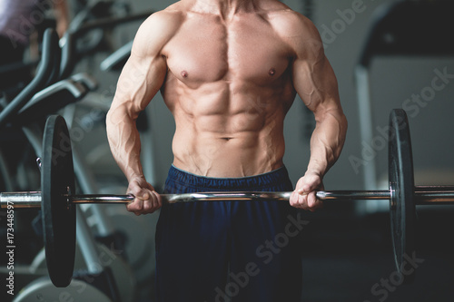 Strong man with muscular body working out in gym. Weight exercise with barbell in fitness club. Toned image