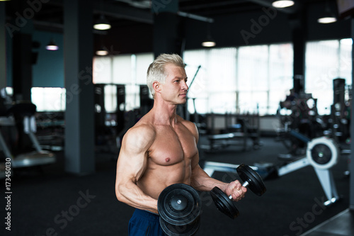 Bodybuilder showing his great body and holding dumbell. Strong man working out in gym.