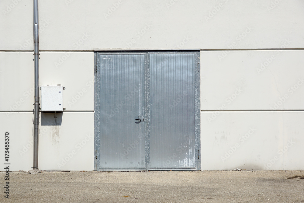 White Overhead Steel Garage Door On Exterior Of Beige Metal Building With Red Bumper Posts