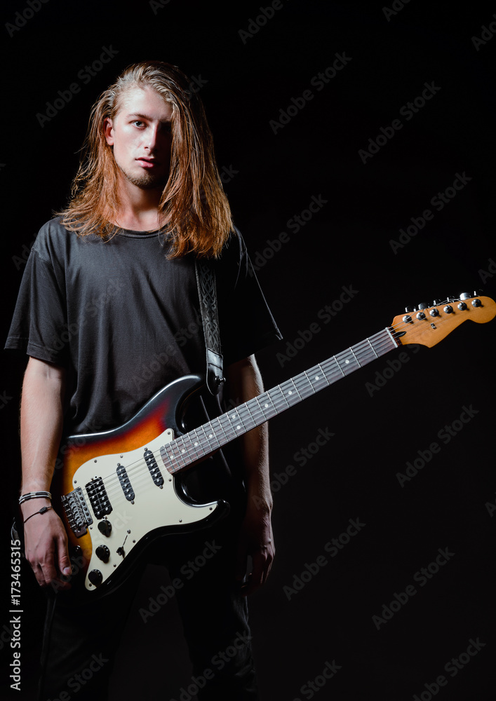 Dramatic studio portrait: handsome longhaired young man (rock musician) with electric guitar Dramatic studio portrait: handsome longhaired young man (rock musician) with electric guitar