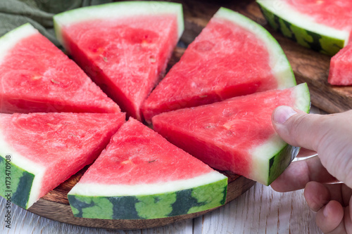 Woman hand take slice of fresh seedless watermelon cut into triangle shape laying on a wooden plate, horizontal
