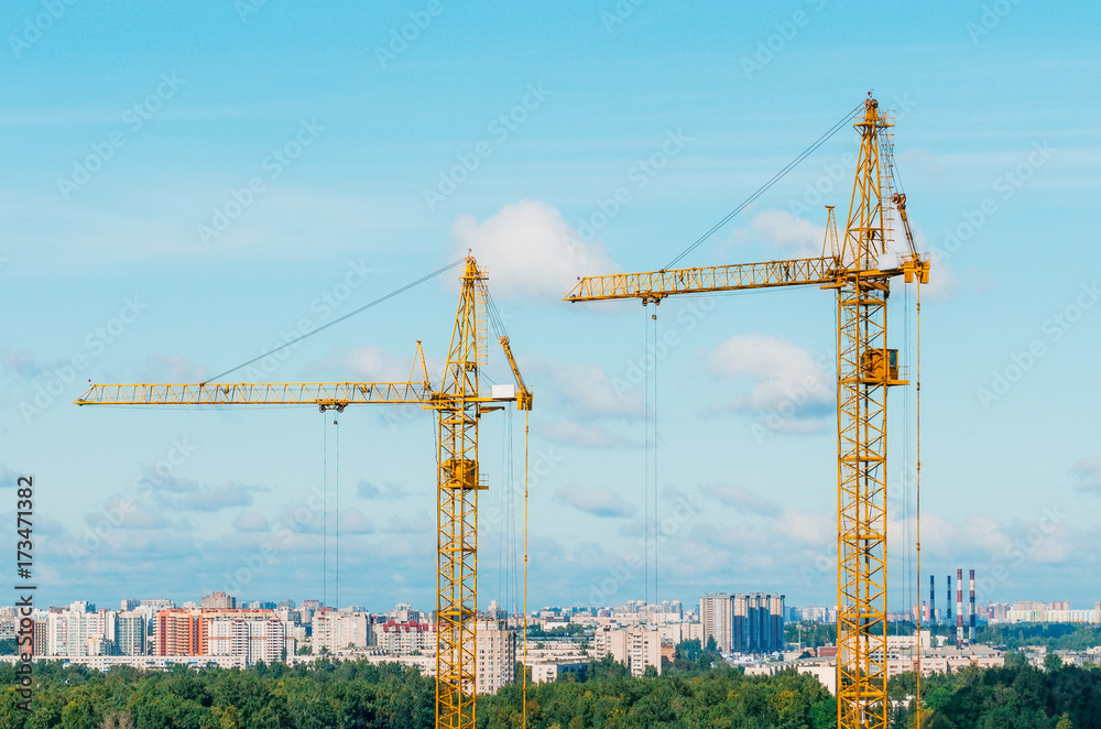 Cranes and housing estate against the background of the city and clouds sky