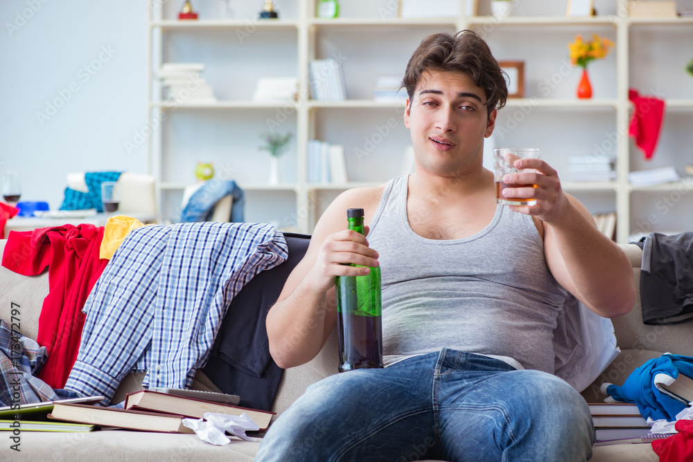 Young man student drunk drinking alcohol in a messy room Young man student drunk drinking alcohol in a messy room