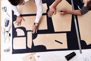 High angle view of concentrated young tailors using sewing patterns while working on creation of custom-made male jacket