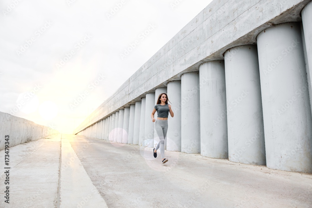 Young attractive woman is running at dawn between concrete walls