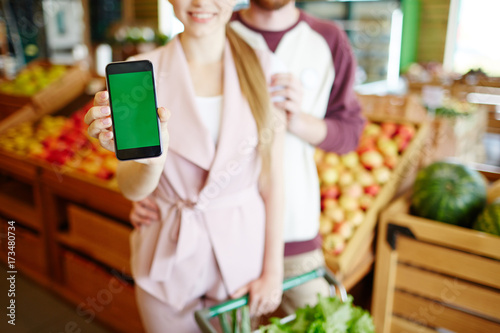 Young female showing online advert in smartphone during shopping in supermarket