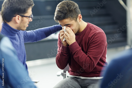 Friendly psychologist reassuring lonely young man in tears during session