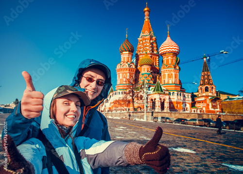 Happy tourists sightseeing city with fingers up next to Saint Basil's Cathedral. Red Square, Moscow, Russia. Holiday, travel, recreation. Winter season, bright colors, clear blue sky