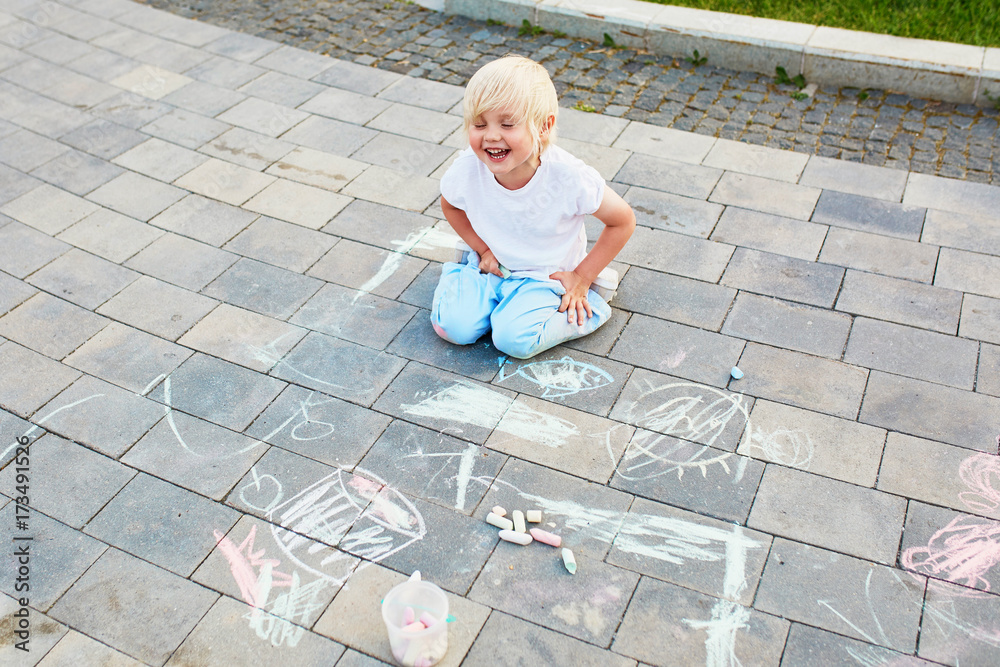 Fototapeta premium Little boy drawing with chalks on asphalt