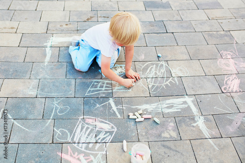Little boy drawing with chalks on asphalt