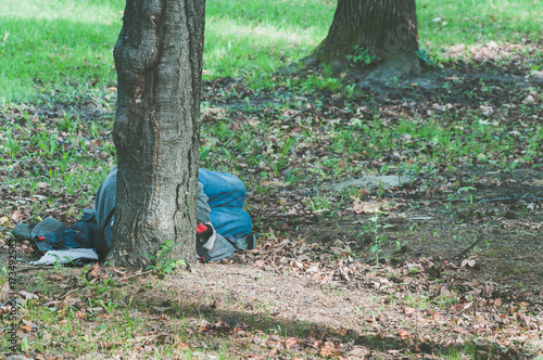 Poor homeless refugee man sleeps on the ground of the park in the city