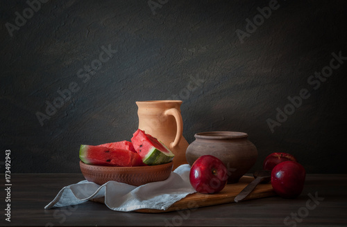 Rustic still life. A set of pottery, red apples and a watermelon on a wooden table