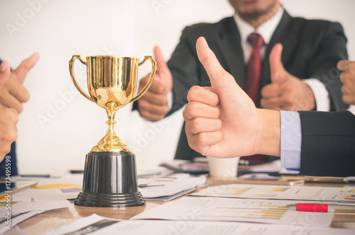 Businessman with colleagues achieve target and successful showing award trophy and thumb up
