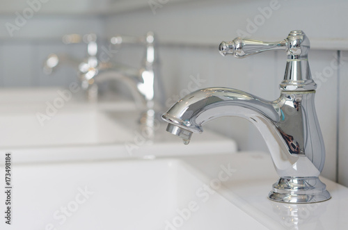 silver faucet or water tap with white washing sink in public toilet.