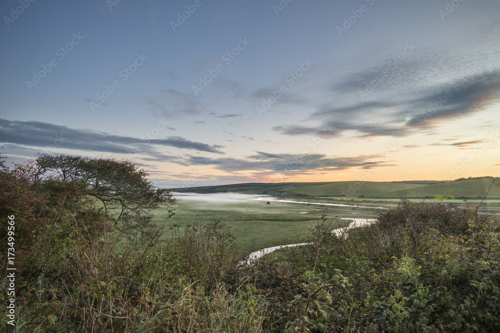 Beautiful dawn landscape over English countryside with river slowly flowing through fields