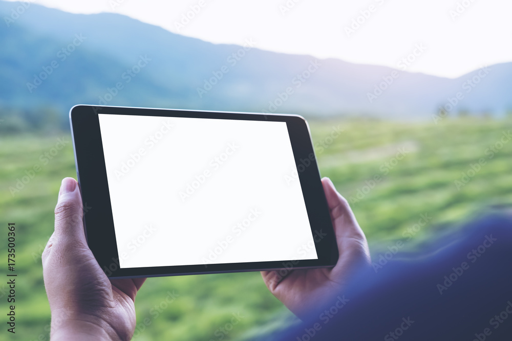 Mockup image of woman's hands holding black tablet pc with blank white screen and green nature background