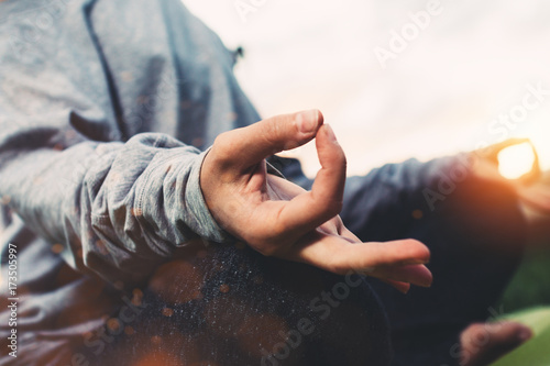 Close up view of female hands in meditation pose. Young girl practicing yoga in urban environment at sunset after a hard day. Concept of relaxation and rest in city park. Blurred background, flares