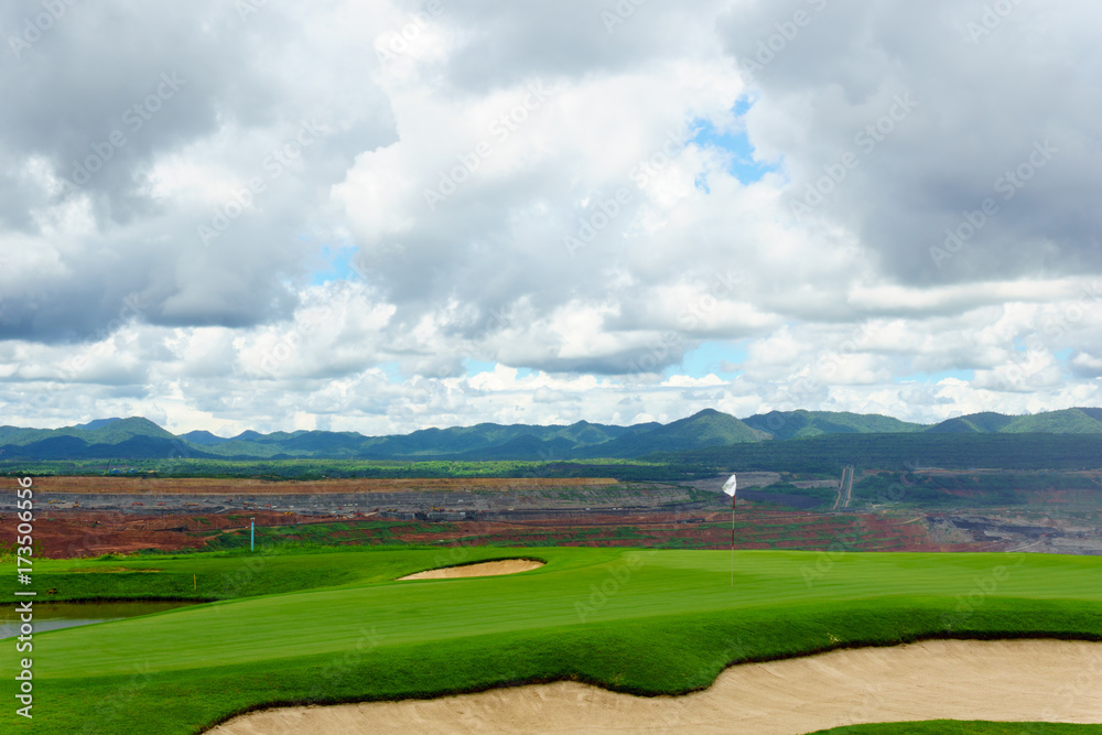 beautiful idyllic view green with sand trap and white flag and view of mountain, blue sky with clouds