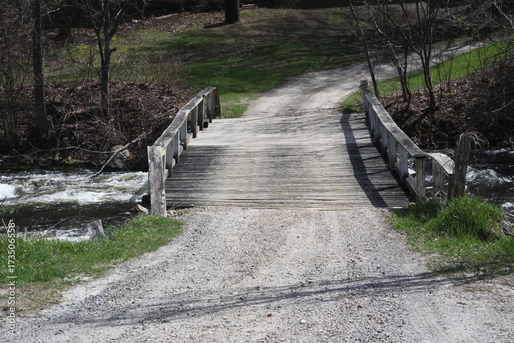 Fototapeta premium Wooden bridge spanning a fast moving creek full of water. 