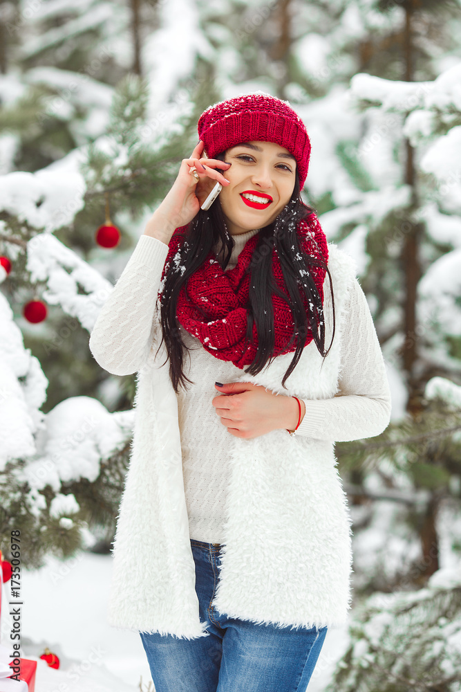 Pretty woman talking on a mobile phone and holding christmas presents. Cheerful young girl smiling a side of camera outdoors Pretty woman talking on a mobile phone and holding christmas presents. Cheerful young girl smiling a side of camera outdoors