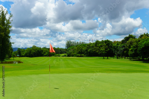 beautiful idyllic view of green with red flag and view of forest, blue sky with clouds.