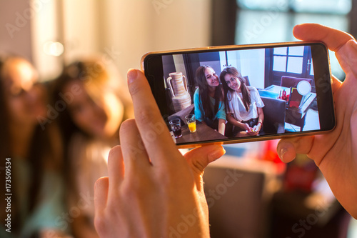 Close up of female hands with mobile phone taking photograph of two smiling teenage girls. photo