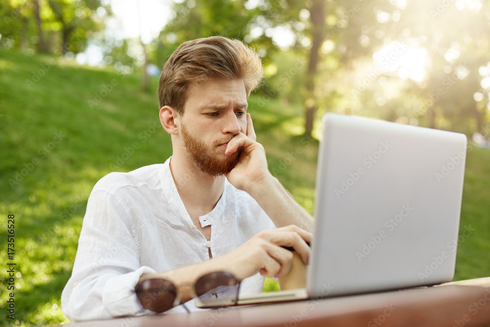 Portrait of thoughtful attractive european man with stylish haircut looking in laptop monitor being upset about new unsuccessful project. Portrait of thoughtful attractive european man with stylish haircut looking in laptop monitor being upset about new unsuccessful project.