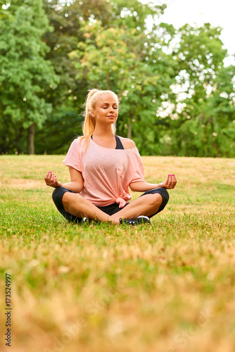 Young woman meditating on a field in a park